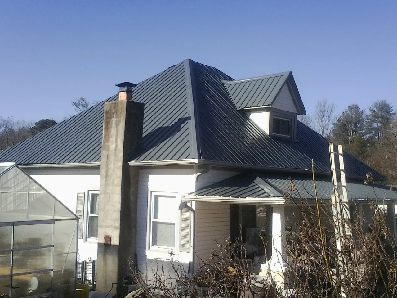 Dark blue standing seam metal roof on a white farmhouse with dormer — Slate & Tile Roof Repair by Roofing Brothers in South New Berlin