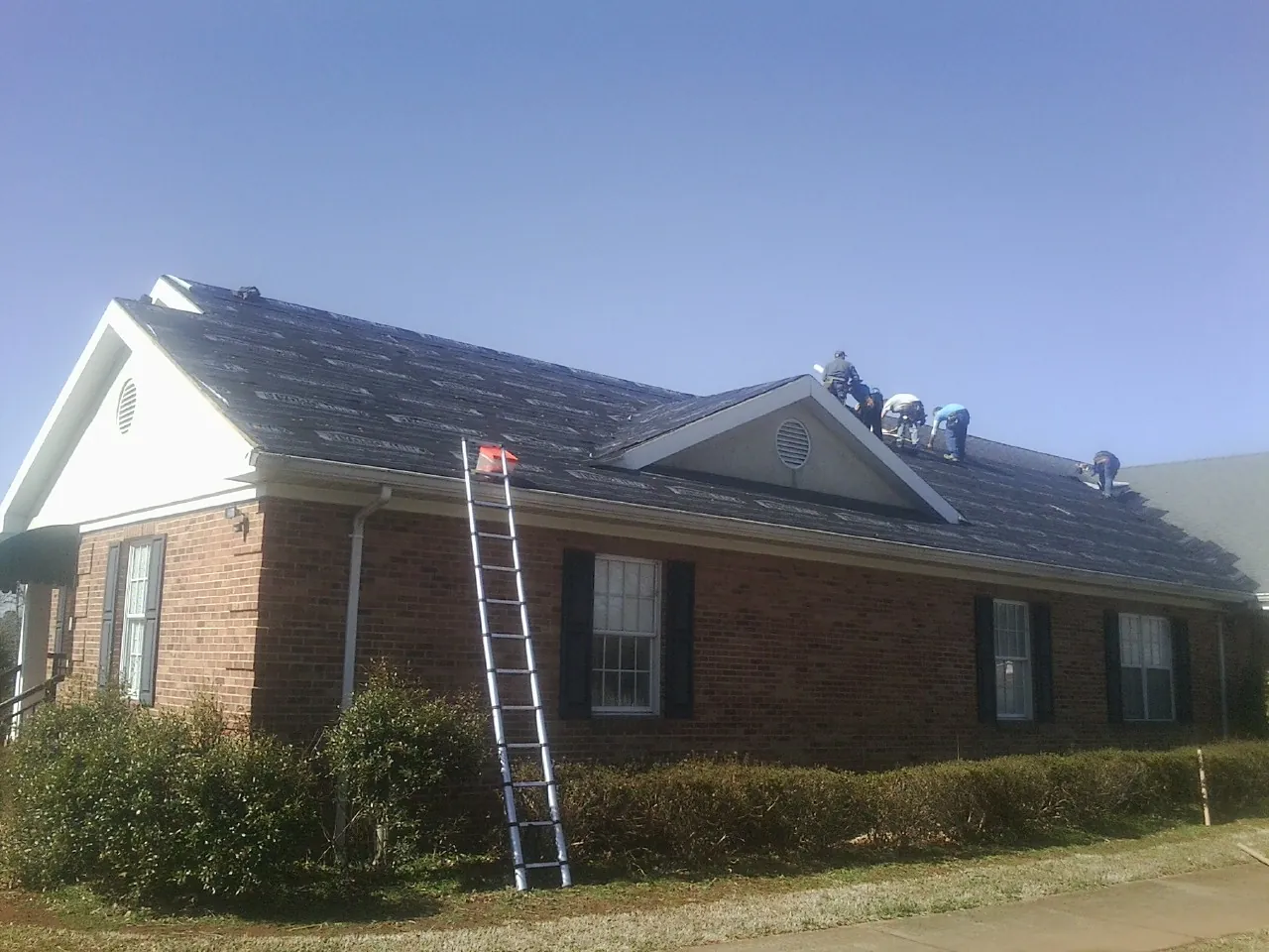 Crew tearing shingles off a brick ranch roof with a ladder set — Emergency Roof Repair work by our crew in South New Berlin