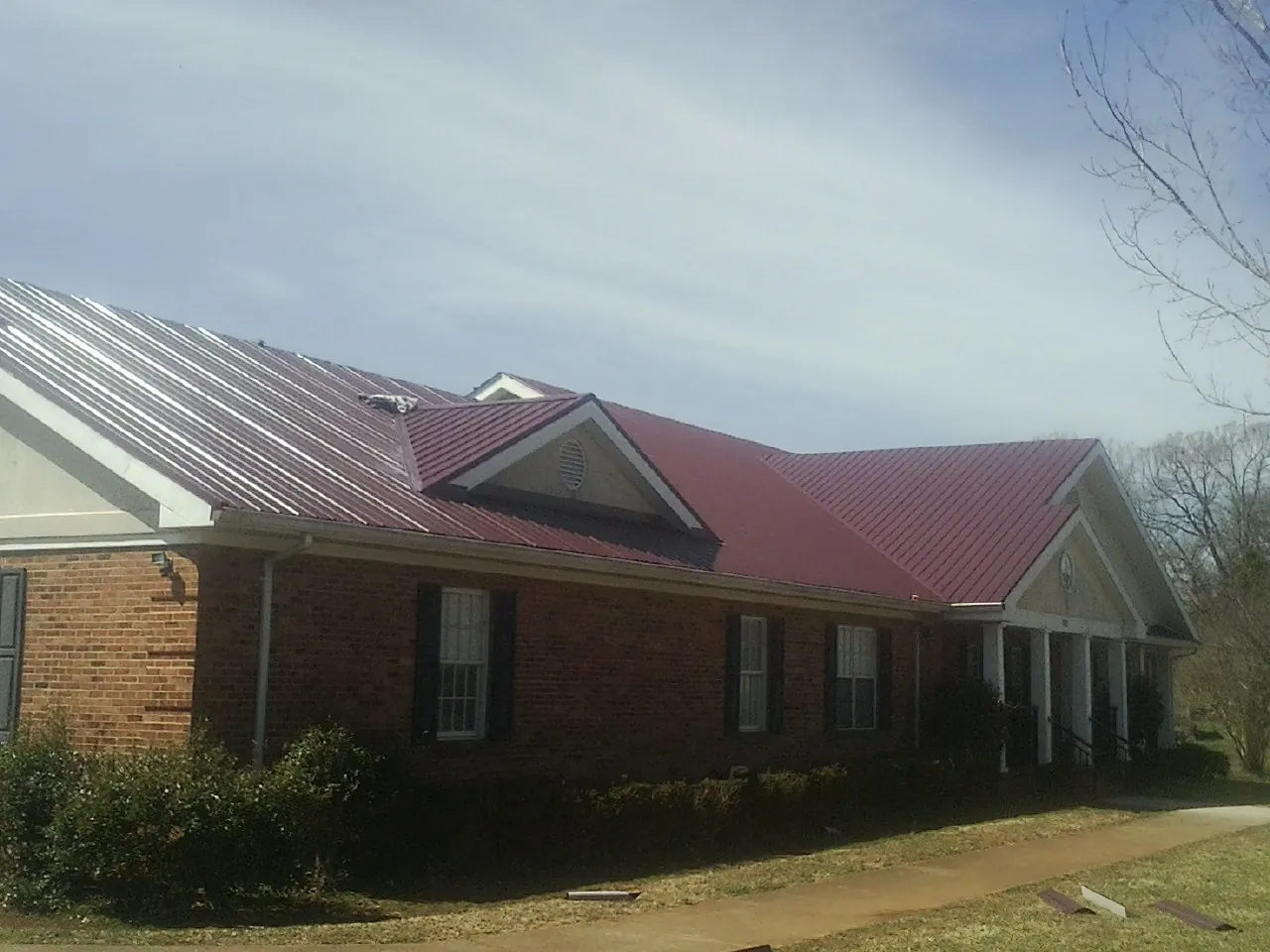 Red metal roof with gabled entries on a long brick building, from a Hail Damage Roof Repair job in South New Berlin