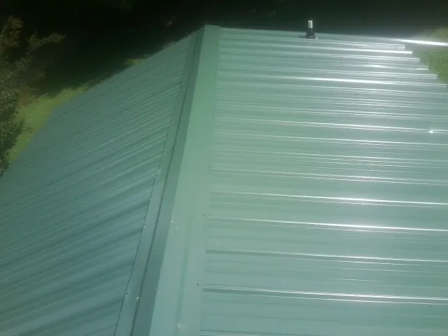 New green metal panels meeting at the ridge of a roof — Flat Roof Repair work by our crew in South New Berlin