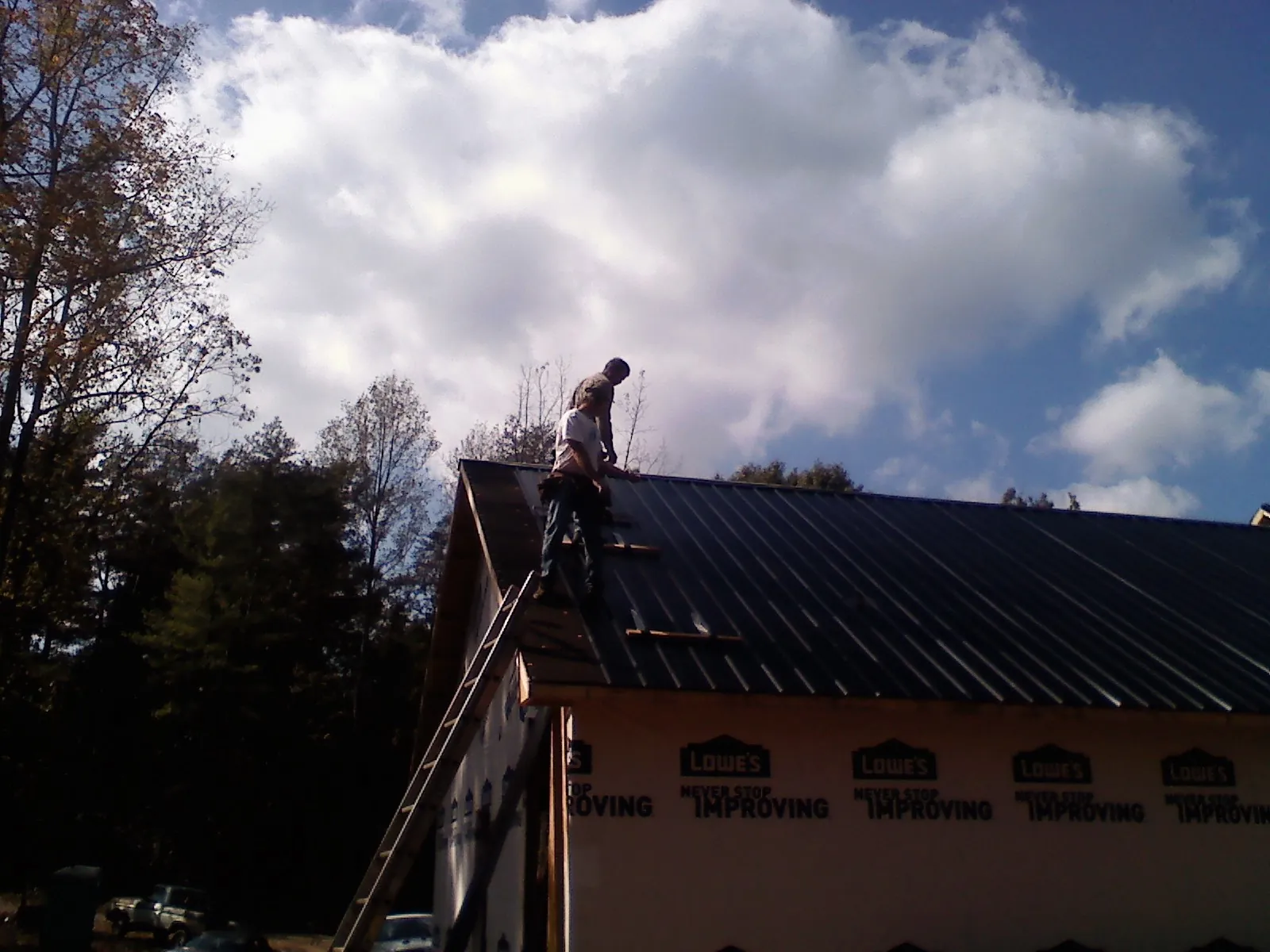 Roofer fastening dark metal panels high against a cloudy sky, from a Roof Inspection job in South New Berlin