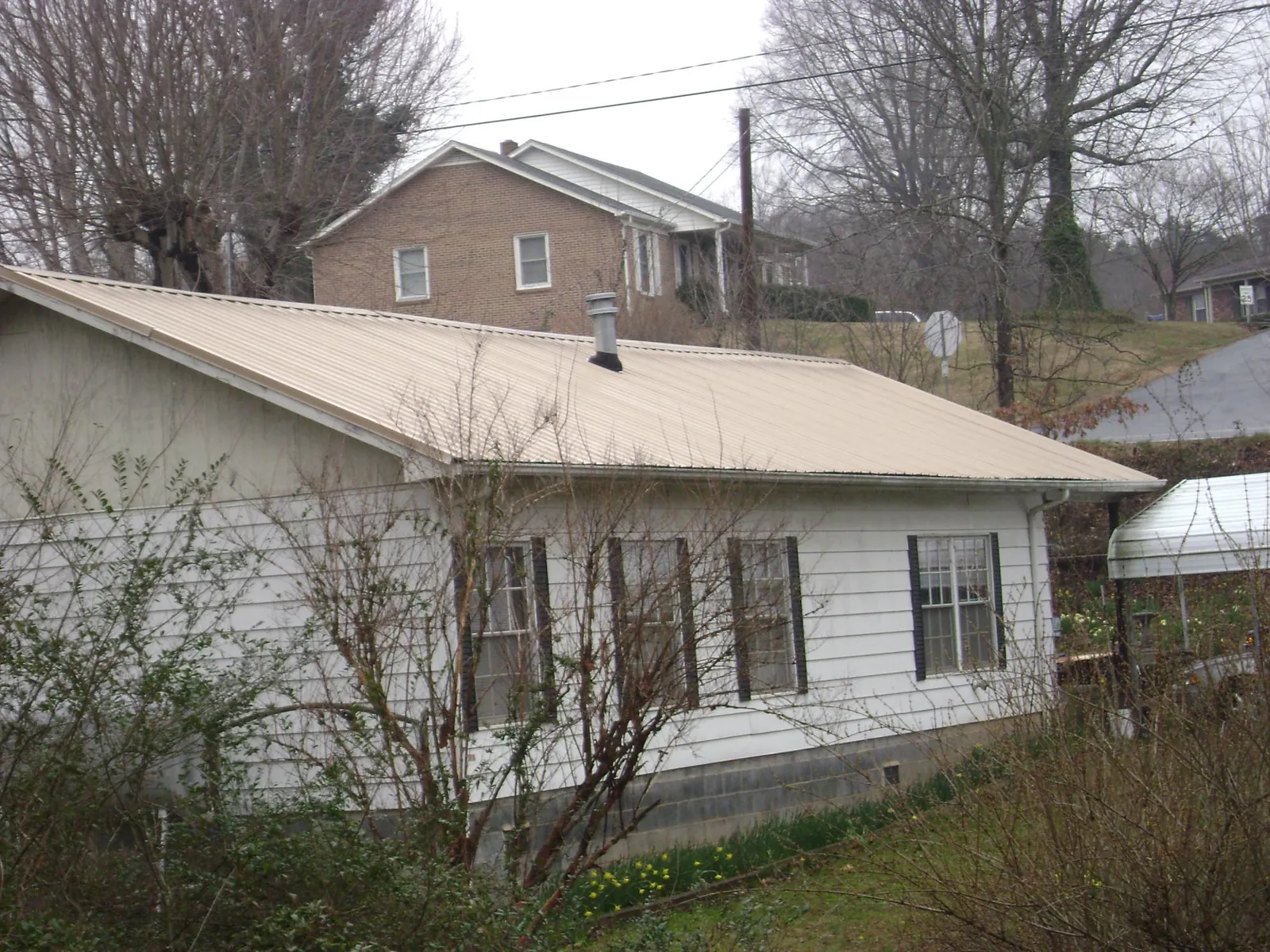 Tan metal roof on a white sided house set into a hillside — Commercial Roofing by Roofing Brothers in South New Berlin